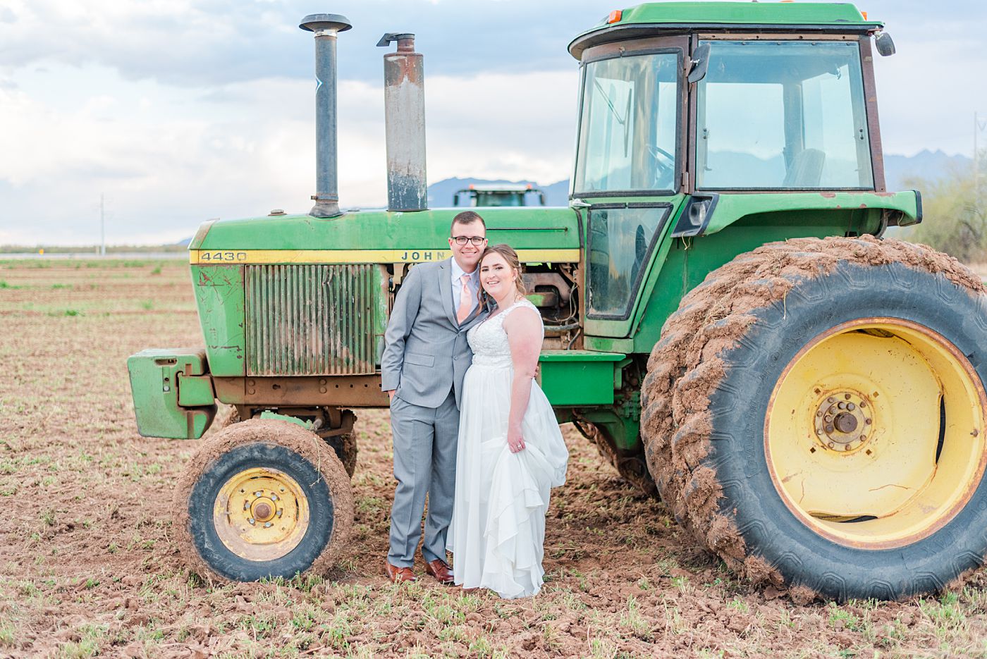 man in suit and woman in white dress standing by a green tractor