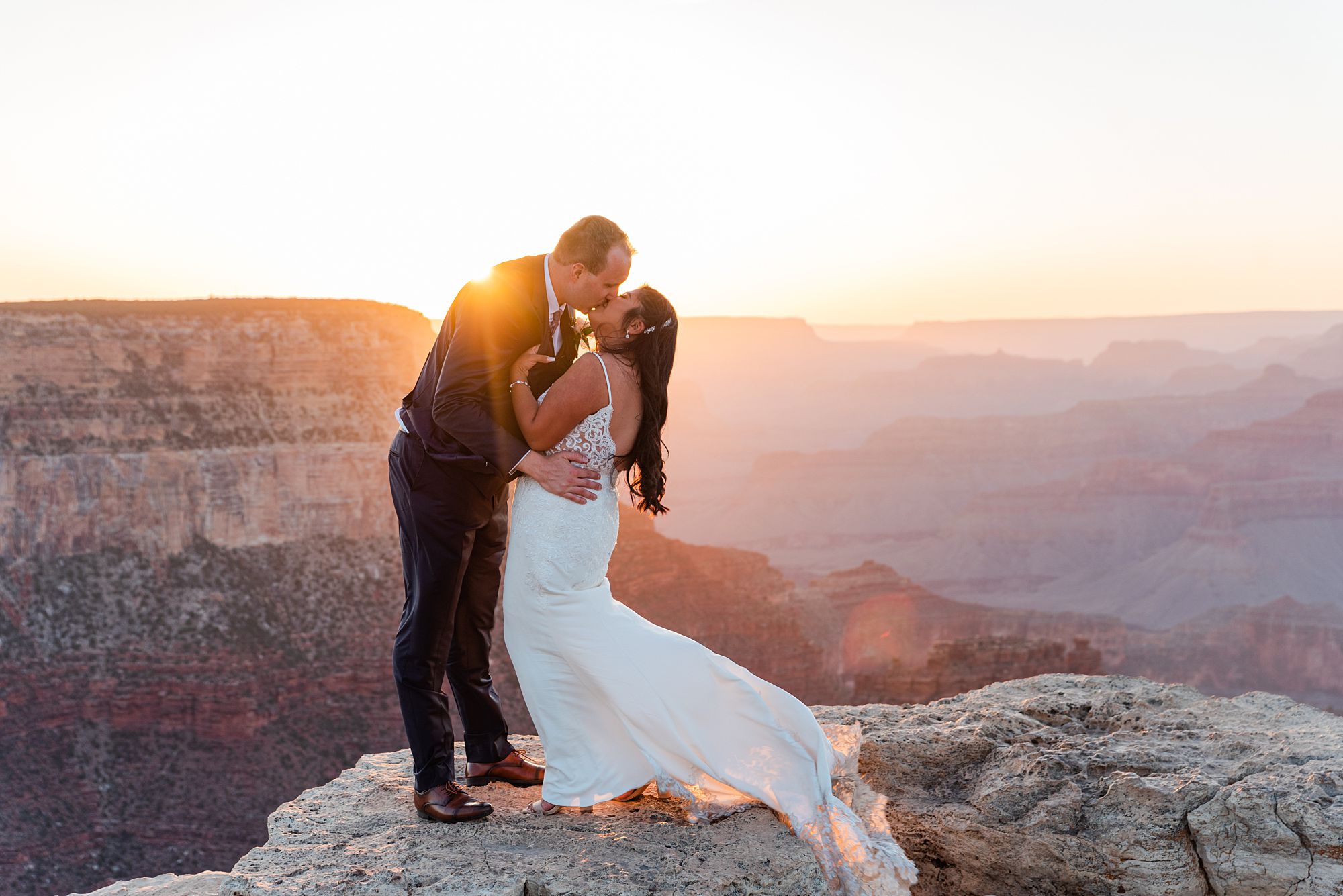 man and woman in a wedding dress kissing during a sunset