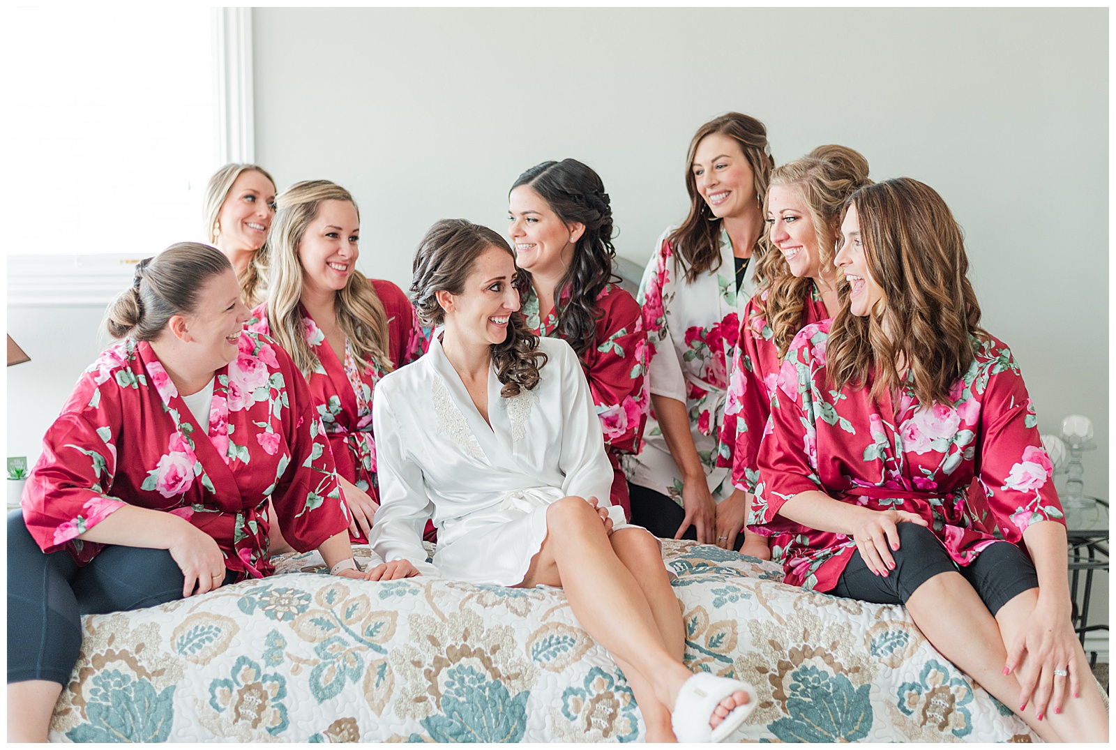 group of women sitting on a bed in pink robes laughing