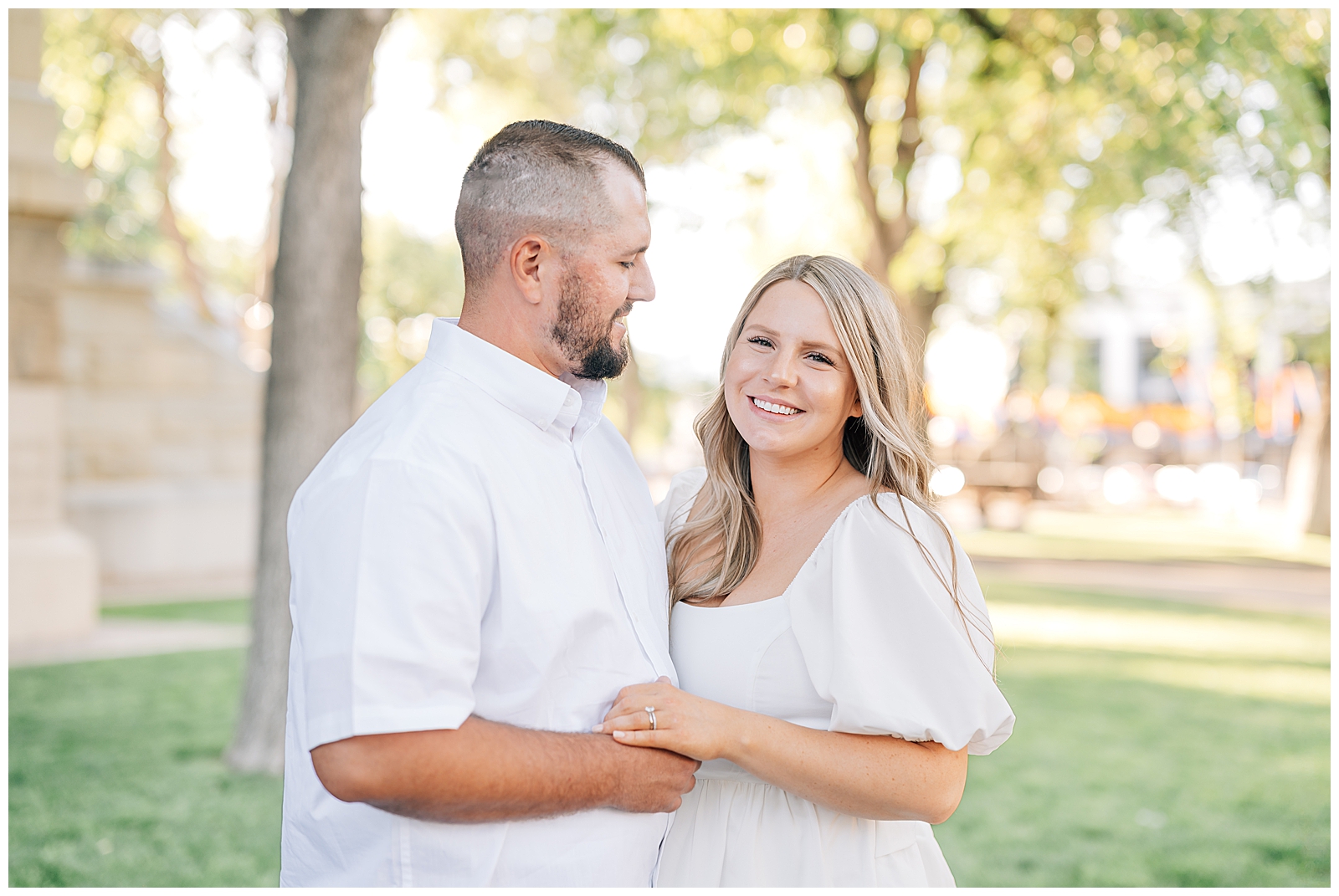 man and wife wearing white standing smiling and standing on green grass in park